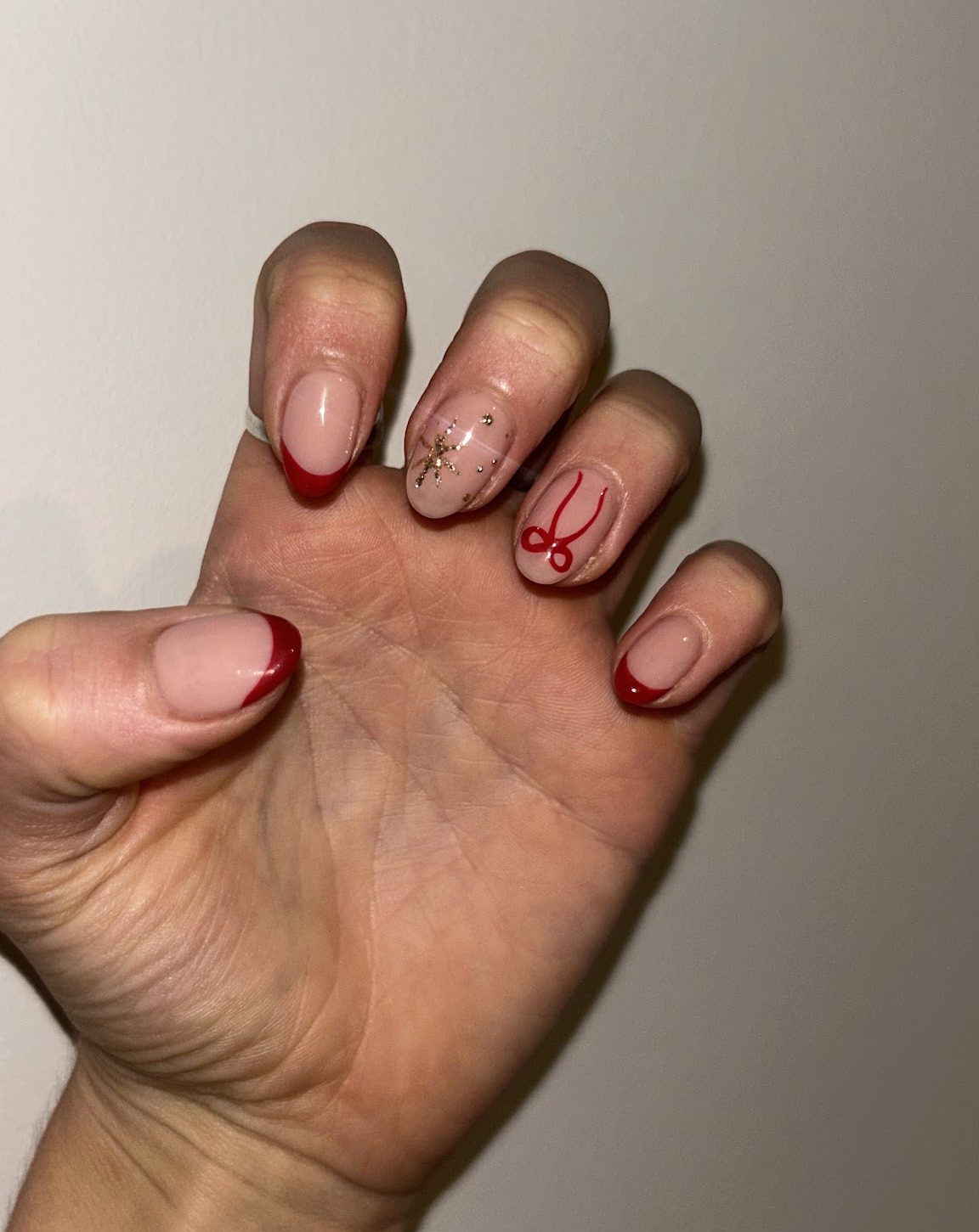 Cherry-red French tips with a gold sparkle star and a hand-painted red Lumière initial, done at Lumière Nail in Dalston