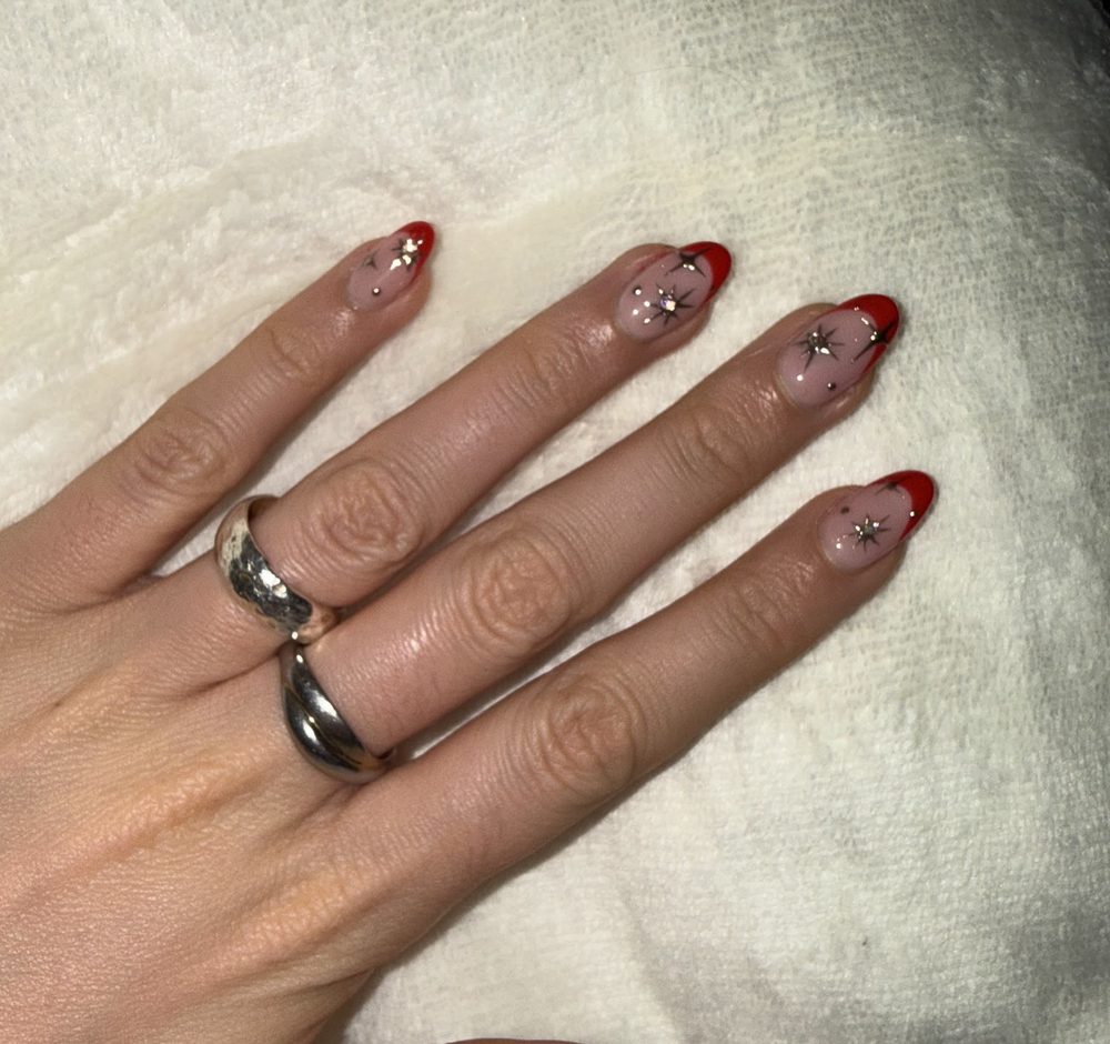 Red French tips with tiny gold and silver star accents on almond nails